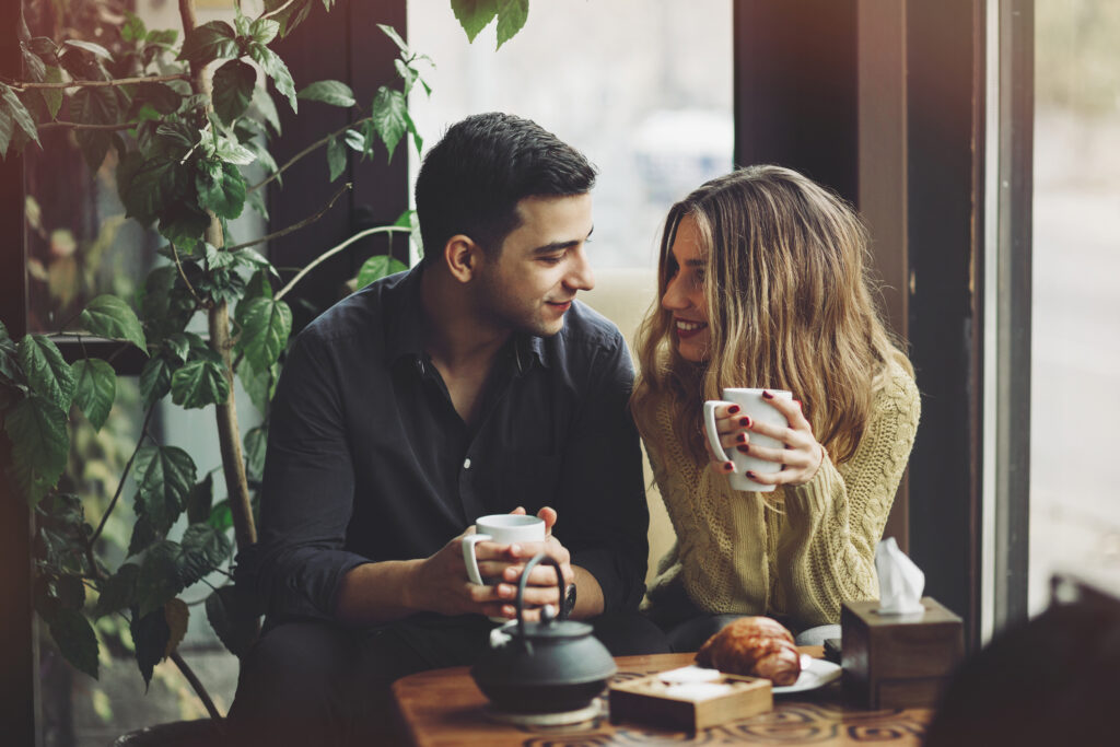 Een man en een vrouw die koffie drinken en glimlachen naar elkaar.
